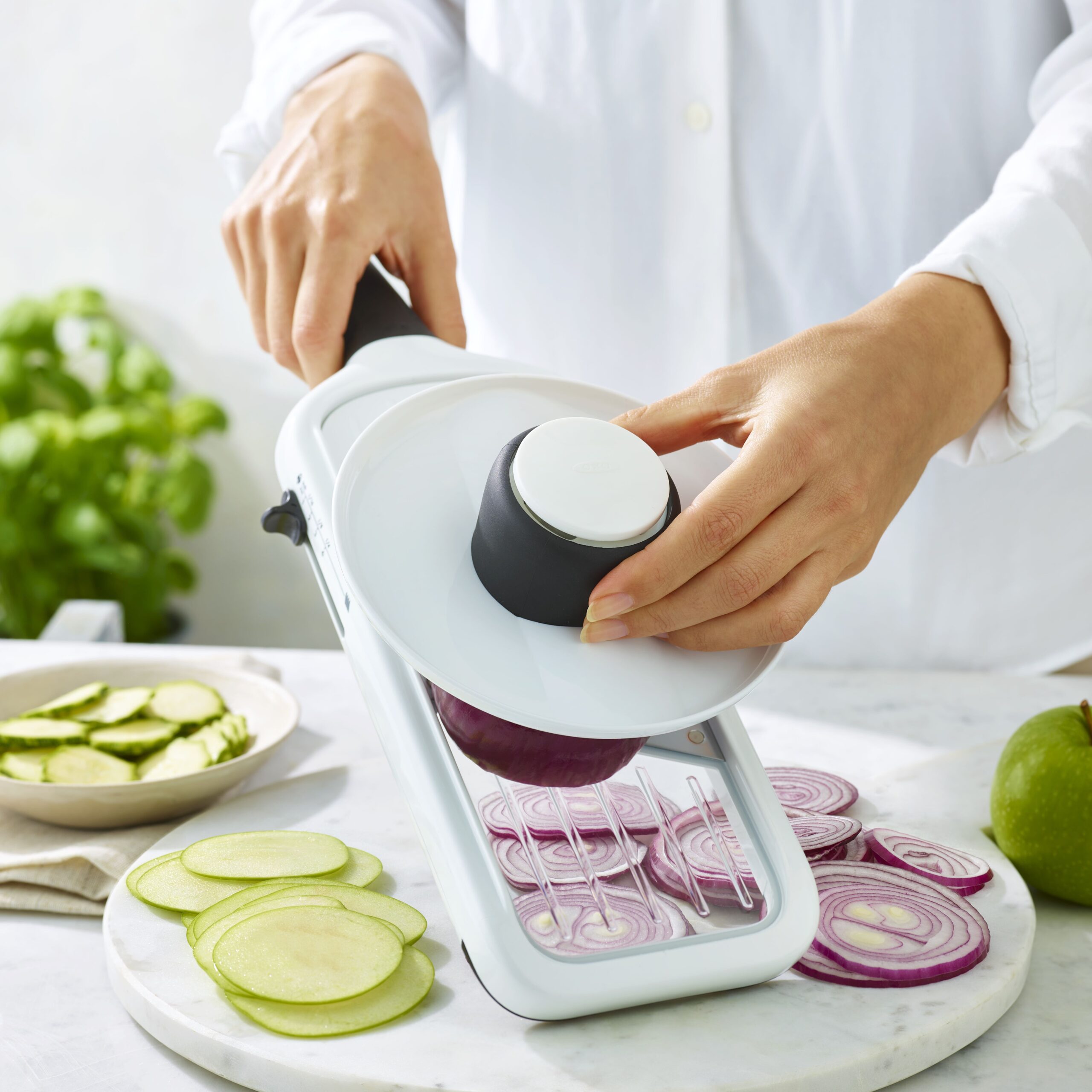The OXO Good Grips Precision Handheld Mandoline in action, slicing red onions in a kitchen worktop setting.
