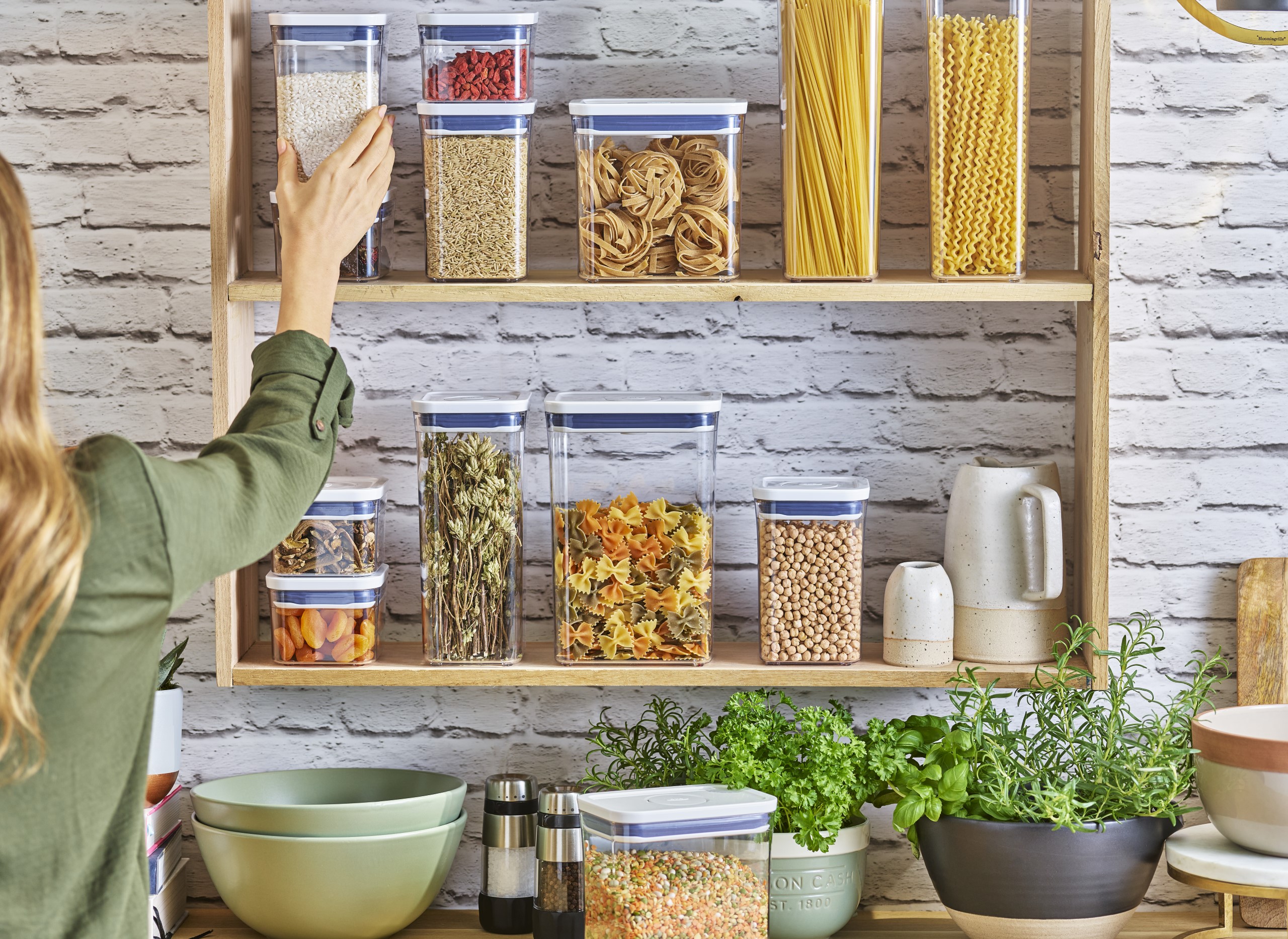 OXO POP Containers being arranged on open wooden shelves in a contemporary kitchen environment.