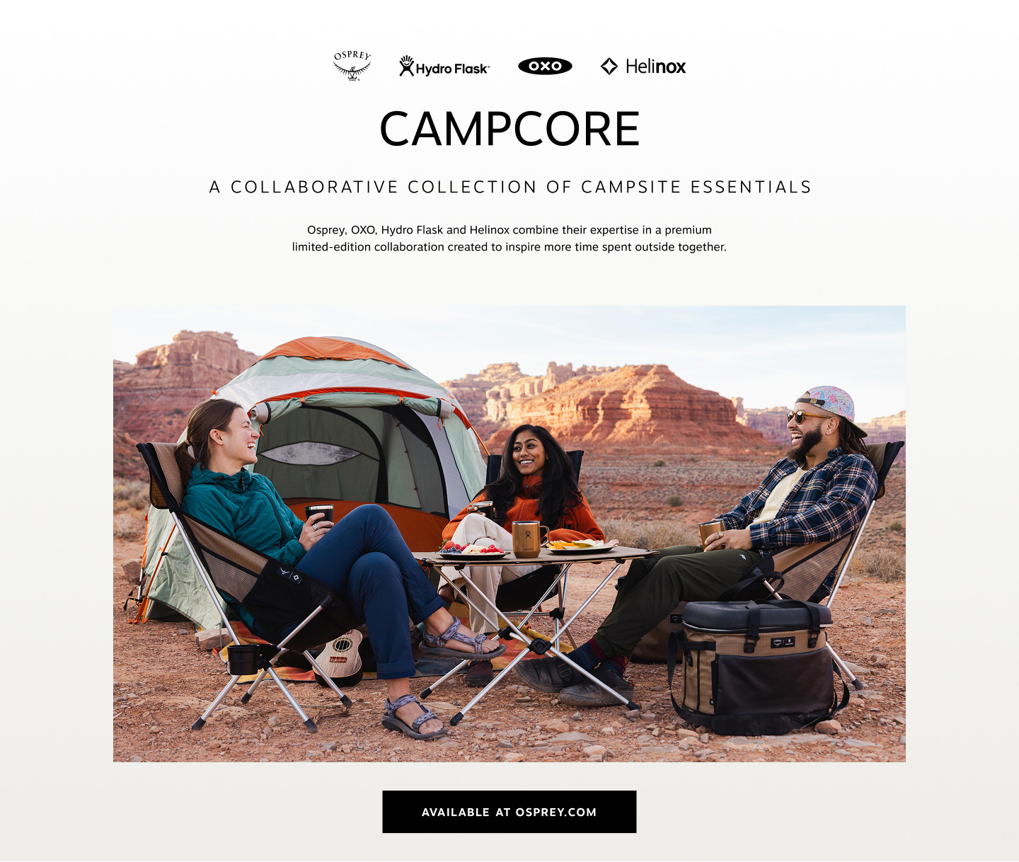 Three people sitting around a foldable camping table in front of a tent, laughing with mugs in hand.